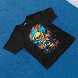 May include: Black t-shirt featuring a graphic of a gold trophy and a flag with blue, yellow, red, and gold colors. The design has a splash of orange and blue paint.