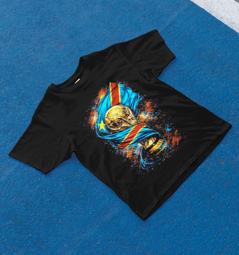 May include: Black t-shirt featuring a graphic of a gold trophy and a flag with blue, yellow, red, and gold colors. The design has a splash of orange and blue paint.
