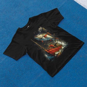 K&ouml;nnte beinhalten: Schwarzes T-Shirt mit einer detaillierten Illustration eines Fisches, der aus dem Wasser springt, in der N&auml;he eines roten Bootes mit einer Person darin. Das Kunstwerk hat ein Vintage-Nautik-Thema mit Fokus auf Angeln und Meer.