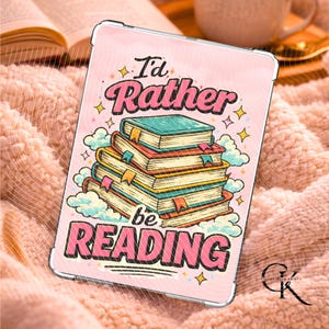 May include: A pink tablet case with the text "I'd Rather be READING" in a retro font. The case features a stack of books with colorful covers and ribbons, surrounded by clouds and stars. The case is on a soft, pink, textured surface.