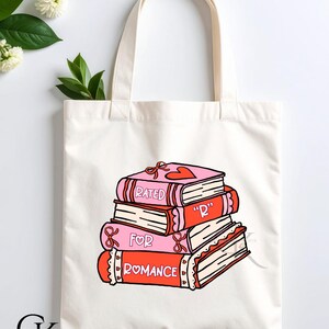 May include: Cream-colored tote bag featuring a stack of illustrated books. The books are pink and red, with the words "RATED", "R", and "FOR ROMANCE" on the spines. Each book has a heart and bow design.