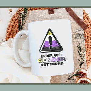 以下が含まれることがあります： 白いセラミックマグカップ、ハンドル付き、非バイナリプライドフラッグのデザインが警告三角形の中にあります。「ERROR 404: GENDER NOT FOUND」のテキストが下にあります。 マグカップは編まれた籐のトレイに置かれています。
