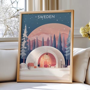 May include: A framed art print featuring a winter landscape scene with the word "SWEDEN" at the top. The artwork depicts a snow-covered area with a domed structure, pine trees, and a pink and blue sky.