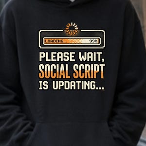 May include: A black hooded sweatshirt featuring a graphic print of a loading bar at 99 percent with the text "PLEASE WAIT, SOCIAL SCRIPT IS UPDATING..." in a pixelated font. The hoodie includes a front kangaroo pocket and long sleeves.
