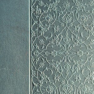 May include: Close-up of a teal-colored book cover with a textured leather-like finish on the left and an embossed floral pattern on the right. The floral design is in a lighter shade, creating a subtle contrast.