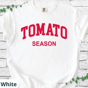 K&ouml;nnte beinhalten: Wei&szlig;es T-Shirt mit dem Text "TOMATO SEASON" in roten, fetten Buchstaben. Der Text ist oben auf dem T-Shirt gebogen. Das Shirt hat einen Rundhalsausschnitt und ist aus weichem Material.