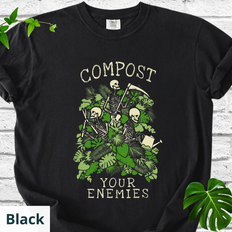 Peut inclure: T-shirt noir avec un motif de trois squelettes dans un feuillage vert, tenant une faux et un arrosoir. Le texte "COMPOST" est au-dessus de l'image et "YOUR ENEMIES" en dessous.