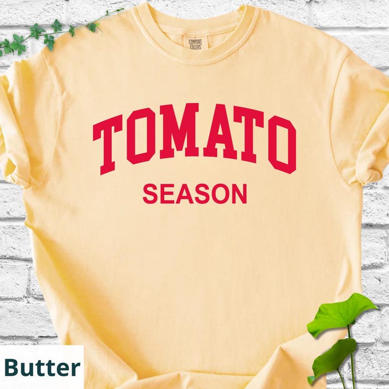 K&ouml;nnte beinhalten: Hellgelbes T-Shirt mit dem roten Schriftzug "TOMATO SEASON". Das T-Shirt hat kurze &Auml;rmel und einen Rundhalsausschnitt. Der Text ist mittig auf der Vorderseite des Shirts platziert.