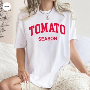 K&ouml;nnte beinhalten: Ein wei&szlig;es T-Shirt mit dem roten Aufdruck "TOMATO SEASON". Das Shirt hat einen l&auml;ssigen Stil mit kurzen &Auml;rmeln und einer lockeren Passform. Der Text ist mittig auf der Vorderseite des Shirts platziert.