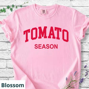 K&ouml;nnte beinhalten: Hellrosa T-Shirt mit dem roten Aufdruck "TOMATO SEASON". Das T-Shirt hat hochgekrempelte &Auml;rmel und besteht aus einem weichen Stoff. Die Farbe des T-Shirts ist Blossom.