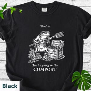 May include: Black t-shirt featuring a frog illustration holding a pitchfork, with the text "That's it." above and "You're going in the COMPOST" below. The frog wears an apron and stands near a wooden chest.