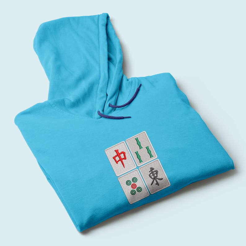 May include: A light blue hoodie with a drawstring hood. The hoodie features four embroidered Mahjong tile designs in red, green, and black. The hoodie is made of a soft material.