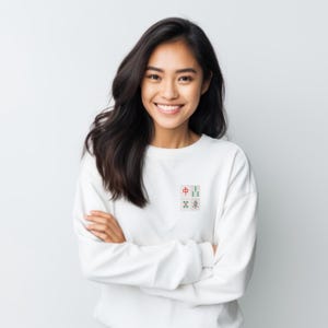 May include: White sweatshirt with a small embroidered design featuring four Mahjong tiles. The tiles are in red, green, and gray colors. The sweatshirt is a simple, casual style.