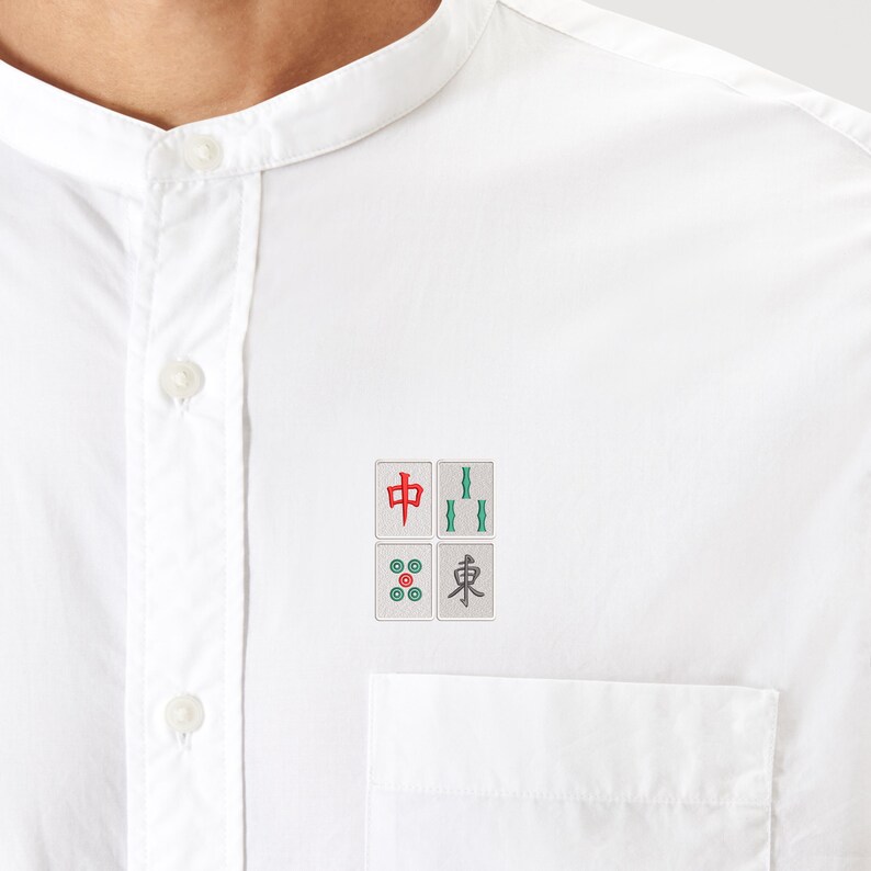 May include: A white shirt with a mandarin collar. The shirt features four embroidered Mahjong tiles on the chest pocket. The tiles are in red, green, and gray, with Chinese characters and symbols.