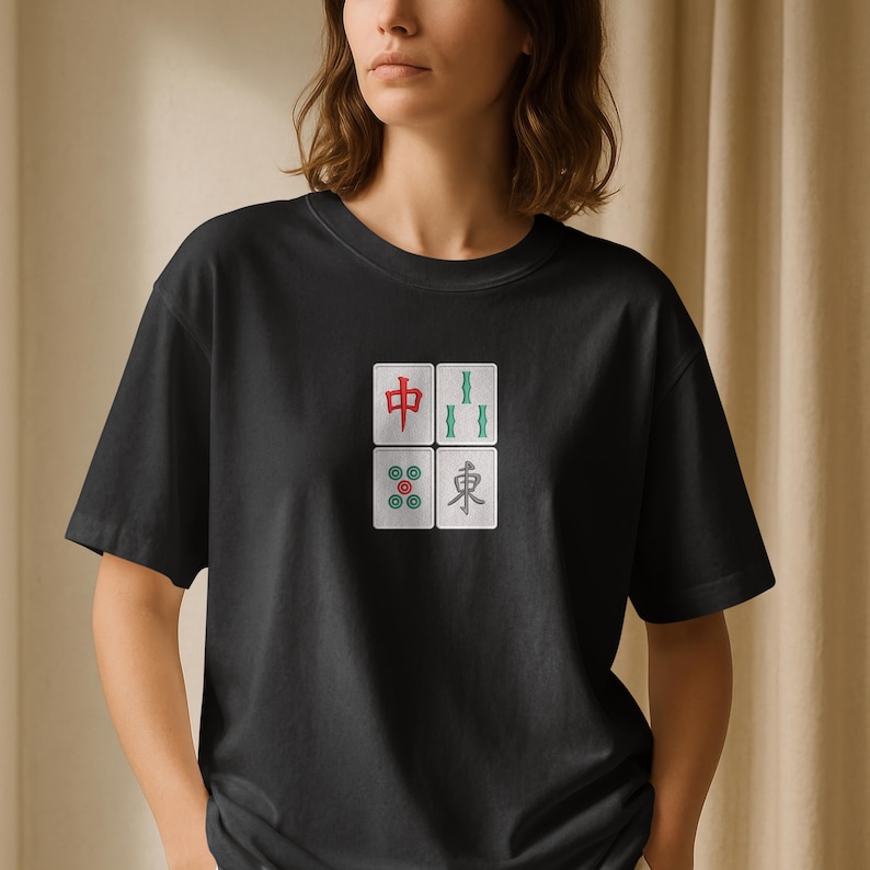 May include: Black t-shirt featuring four embroidered Mahjong tiles in red, green, and teal. The tiles are arranged in a square pattern on the front of the shirt. The shirt has short sleeves and a crew neck.