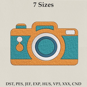 Op de afbeelding: Een geborduurd cameradesign in oranje en blauwgroen. De afbeelding bevat bovenaan de tekst "7 Maten" en onderaan borduurformaatbestanden. De camera heeft een cirkelvormige lens en een rechthoekige behuizing.