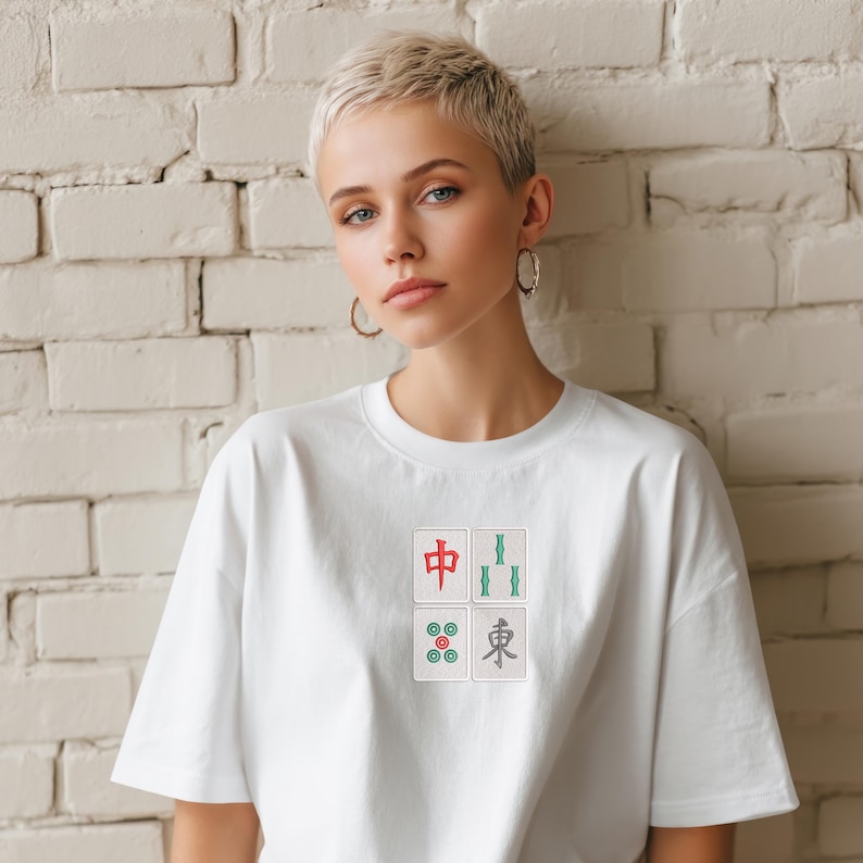 May include: White t-shirt with a small embroidered design featuring four Mahjong tiles. The tiles are in red, green, and gray, with Chinese characters and symbols. The shirt is a casual, unisex style.