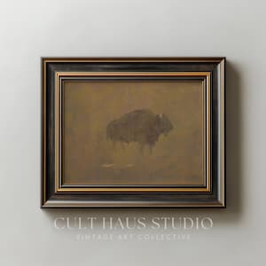 Può includere: Opera d'arte incorniciata con una silhouette di bisonte in tonalità marroni tenui. Il dipinto è racchiuso in una cornice nera con un bordo interno dorato. Il testo "CULT HAUS STUDIO VINTAGE ART COLLECTIVE" è visibile in basso.