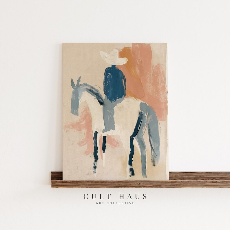 May include: Abstract art print of a person on horseback. The artwork features a cowboy in a white hat and blue shirt riding a white horse with blue accents. The background has pink and peach brushstrokes. The text "CULT HAUS ART COLLECTIVE" is at the bottom.