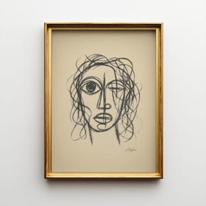 Può includere: Un disegno astratto a carboncino incorniciato di un volto con un occhio aperto e uno chiuso. L'opera d'arte è in una cornice dorata e firmata in basso a destra. Il disegno è su uno sfondo beige.