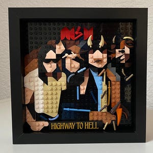 Puede incluir: Una obra de arte enmarcada que presenta un retrato de una banda construido con bloques de construcción coloridos. Los miembros de la banda están representados de forma estilizada, con el nombre de la banda en la parte superior y la frase "HIGHWAY TO HELL" en la parte inferior. El marco es negro.