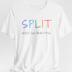 Puede incluir: Una camiseta blanca de manga corta con la palabra SPLIT en letras multicolores y el texto CRAZY but BEAUTIFUL impreso en negro debajo. La prenda cuenta con un cuello redondo y un corte estándar que presenta un diseño sencillo.