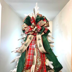 May include: A festive Christmas tree bow featuring a mix of ribbons in red plaid, green, and beige with Christmas tree and floral patterns. The bow is large and decorative, perfect for holiday decorating.