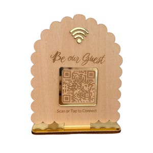 Może przedstawiać: Drewniany znak z falistą krawędzią, z pozłacanym symbolem Wi-Fi i kodem QR. Tekst "Be our Guest" jest napisany nad kodem QR, a pod nim "Scan or Tap to Connect".