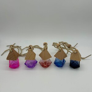 May include: Five colourful, geometric-shaped glass bottles with wooden tops and twine cords. The bottles are in shades of pink, purple, red, blue, and black. The bottles are likely for essential oils or perfumes.