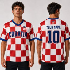 Puede incluir: Una camiseta de manga corta con cuello en V y un patr&oacute;n de cuadros rojos y blancos. El frente muestra el texto "CROATIA" en azul con un peque&ntilde;o escudo. La parte posterior muestra el texto "YOUR NAME" sobre el n&uacute;mero "10" en azul con escudo.