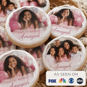 May include: Round sugar cookies with edible printed images featuring a young girl or a family, pink balloons, and the text Happy 8th Birthday Amayah. The cookies have a white piped icing border and are arranged in a woven basket.