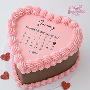 May include: A heart-shaped cake with pink frosting and a calendar for January. The cake has a chocolate base and is decorated with pink frosting swirls around the edges. The calendar highlights the 19th with a heart. The cake is on a white surface.