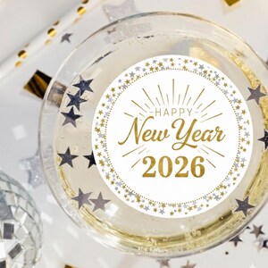 May include: A champagne glass filled with bubbly liquid, featuring a circular sticker with the words "Happy New Year 2026" in gold lettering. The glass is surrounded by star-shaped confetti and a disco ball.