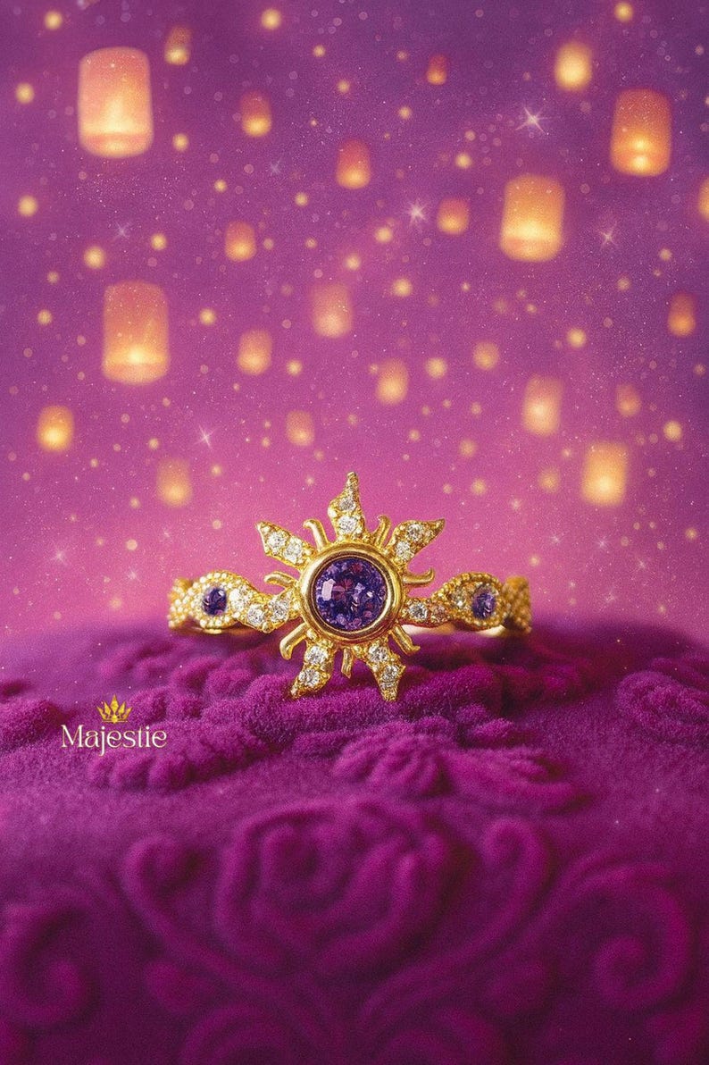 Peut inclure: Une bague en or avec un motif de soleil, orn&eacute;e d'une pierre pr&eacute;cieuse violette centrale et de diamants. La bague est pos&eacute;e sur une surface de velours violet, avec un fond de lanternes flottantes et de lumi&egrave;res scintillantes. Le mot "Majestie" est en bas.