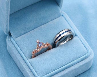Anillos de pareja inspirados en Cenicienta: corona de oro rosa y banda azul plateada a juego.