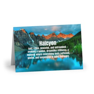 May include: A greeting card with a landscape scene of mountains, a lake, and trees. The word "Halcyon" is displayed in white text, along with its definition: calm, peaceful, and untroubled.