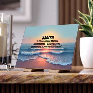 May include: A wooden block with the word "Saorsa" and its definition printed on it. The image shows a beach scene with a sunset, featuring blue water, a pink and orange sky, and the text "freedom and spiritual independence".