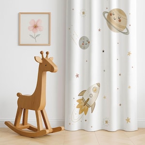 Peut inclure: Un jouet girafe à bascule en bois est placé à côté d'un rideau blanc décoré sur le thème de l'espace. Le rideau présente des planètes, des étoiles et une fusée dans des tons beiges et dorés. Une impression florale encadrée est accrochée au mur.