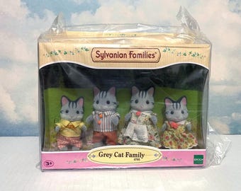 May include: A boxed set of Sylvanian Families Grey Cat Family figurines. The set includes four gray cat figures wearing various outfits, including dresses and shirts. The packaging features the Sylvanian Families logo and the words "Grey Cat Family".
