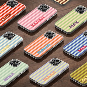 May include: A collection of clear phone cases with colorful striped designs. Each case features a different name in a coordinating color. The cases are arranged on a dark wood surface.