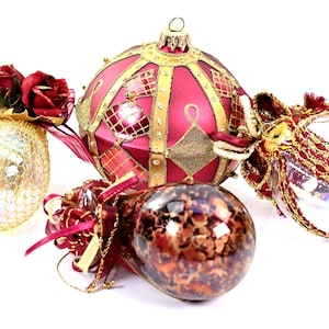 May include: A selection of Christmas baubles. The decorations include a gold mesh ball with red roses, a red and gold patterned bauble, a brown and gold speckled bauble, and a clear bauble with gold trim and red ribbon.