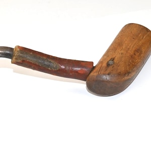 Puede incluir: Una antigua herramienta de gancho con un gancho de metal curvado y un mango de madera. El mango es de color marrón oscuro con una sección pintada de rojo. La herramienta parece desgastada, lo que sugiere edad y uso.