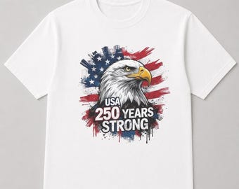 May include: White t-shirt featuring a detailed illustration of an American bald eagle with a yellow beak. The design includes the text "USA 250 YEARS STRONG" over a backdrop of the American flag in red, white, and blue.