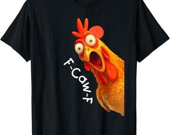 May include: Black t-shirt featuring a cartoon chicken with wide eyes and an open beak. The chicken is orange, yellow, and red, with the text "F-Caw-F" in white. The shirt is a standard crew neck.