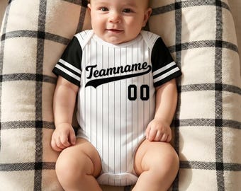 May include: A baby wearing a white and black baseball-themed onesie with the text "Teamname" and the number "00". The onesie has black sleeves with white stripes. The baby is lying on a cream-colored, checkered blanket.