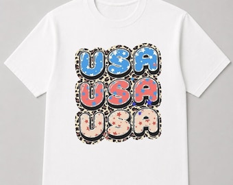 May include: White t-shirt with a graphic design featuring the word "USA" in three rows. Each letter is outlined in black and filled with blue, red, and beige colors, and decorated with stars. The background has a leopard print.