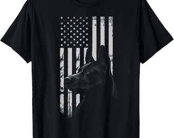 May include: Black t-shirt featuring a distressed American flag design with a black dog silhouette. The dog is a German Shepherd, with a focused gaze. The flag's white stripes and stars contrast against the black fabric.