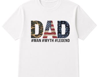 May include: White t-shirt with the word "DAD" in camouflage, American flag, and navy blue star patterns. Below the word "DAD" are the hashtags #MAN #MYTH #LEGEND. The shirt is made of a soft, comfortable material.