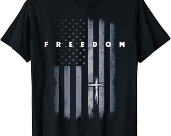 May include: Black t-shirt featuring a distressed American flag design with a white cross and the word "FREEDOM" in white block letters. The flag design has a faded, vintage look.