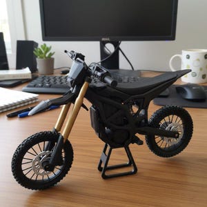 K&ouml;nnte beinhalten: Ein schwarzes und goldenes Miniaturmotorradmodell. Der Sitz, die Reifen und der Rahmen sind schwarz, mit goldenen Vorderradgabeln. Das Motorrad steht auf einem schwarzen St&auml;nder. Auf einem Holztisch.